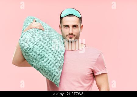 Young handsome man in sleeping mask holding pillow in hands Stock Photo