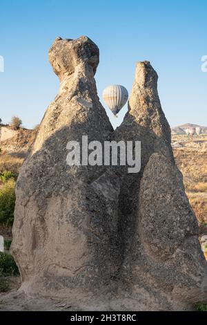 GOREME, TURKEY - AUGUST 5, 2021: One lonely hot air balloon rising in the morning light behind two rock fairy chimneys in Cappadocia Stock Photo