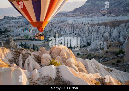 GOREME, TURKEY - AUGUST 3, 2021: Close up of colorful hot air balloons with basket full of tourists flying very close to the ground over the Cappadoci Stock Photo