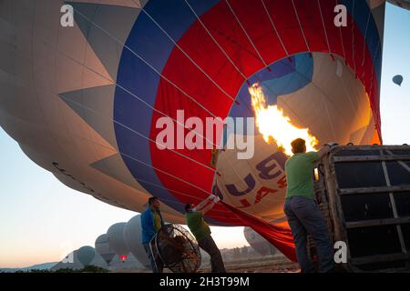 GOREME, TURKEY - AUGUST 3, 2021: People work hard to inflate on the ground a hot air balloon using the warm air from the burner flame so that the tour Stock Photo
