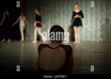 Dance teacher. The choreographer looks at the students. Dance lessons on stage. A girl in a dress with a neckline on her back. Stock Photo