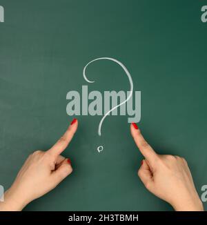 Question mark drawn in white chalk and female hands point a finger at it Stock Photo