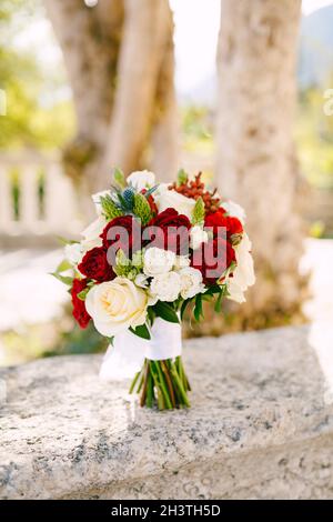 Bridal bouquet of white, read and cream roses, ornithogalum, eryngium with white ribbons on the fence Stock Photo