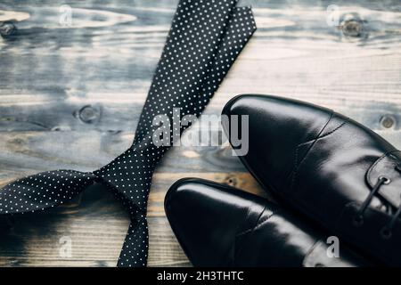 Black tie with white polka dots and men's leather shoes on a wooden background.