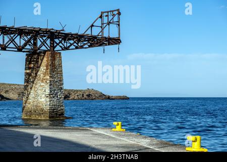 Old rusty mine iron railway bridge supported on stone base and yellow bollards at Loutra port Kythnos island Cyclades summer destination Greece. Land, Stock Photo