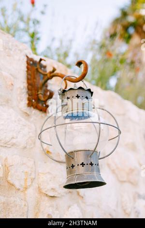 Old metal hanging lantern on a rusty hook on a stone wall. Stock Photo