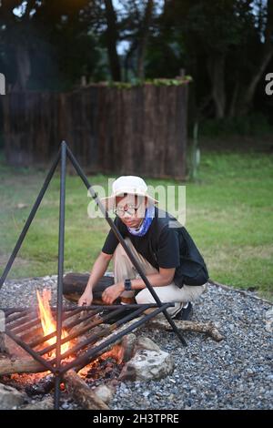 Young man traveler make bonfire  near camping tents in forest. Stock Photo