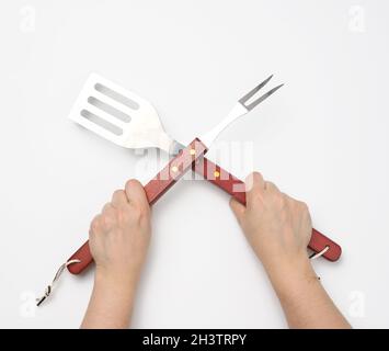 Metal spatula and fork with a wooden handle for a picnic in a female hand with painted red nails on a white background Stock Photo
