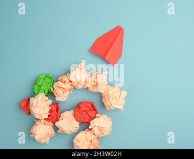 Red paper airplane and crumpled paper balls on a blue background, top view. Stock Photo
