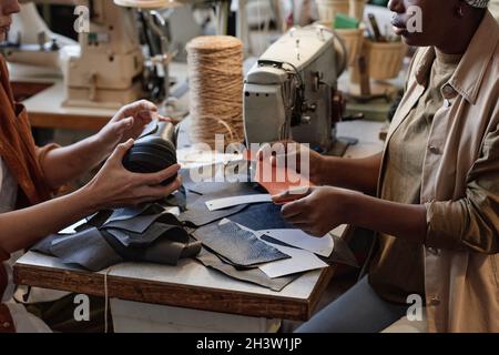 Close-up of two tailors sitting at the table and repairing shoes from pieces of leather in the factory Stock Photo