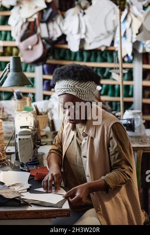African young tailor using patterns to cut clothes at her workplace in the clothes factory Stock Photo
