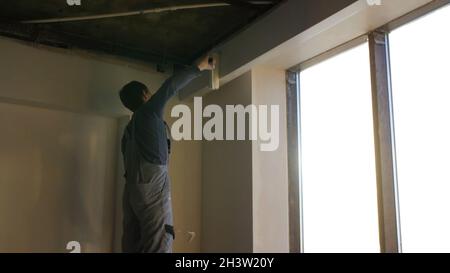 Painter working with paint roller to paint the wall of a room. Do it yourself concept. Man paints the wall with a roller at the window. Stock Photo