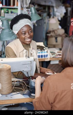 African young tailor smiling to her colleague while they talking during their sewing work in the workshop Stock Photo