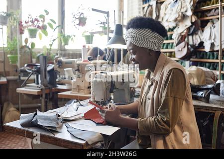 African woman reading a message on mobile phone while she sewing clothes in the factory Stock Photo
