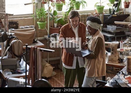 Tailor showing clothes collection online on laptop and discussing it with the customer in the workshop Stock Photo