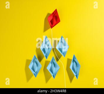 Group of blue paper boats and one red led on a yellow background. Stock Photo