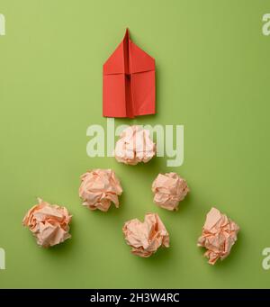 Red paper airplane and crumpled paper balls on a green background, top view. The concept of finding innovative ideas Stock Photo