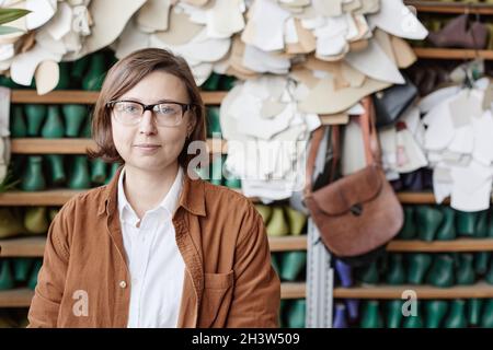 Portrait of mature woman in eyeglasses looking at camera while working as a shoemaker in the factory Stock Photo