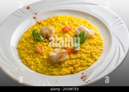 Yellow saffron risotto with cuttlefish, basil leaves and fresh tomato pulp, gourmet recipe in a white dish Stock Photo