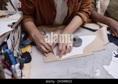 Close-up of tailor drawing pattern on the fabric to cut it and sew details at her workplace in the workshop Stock Photo