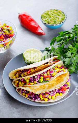 Vegan tacos with corn, purple cabbage and tomatoes on a gray plate. Mexican tacos with vegetables and guacamole on gray background. Close-up Stock Photo