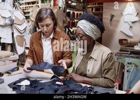 Two tailors sitting at their workplaces and sewing pieces of the fabric in team during their work in the workshop Stock Photo