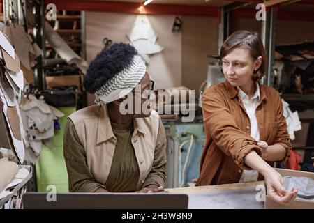Two colleagues sitting at the table with laptop and discussing work together, they working in the clothes workshop Stock Photo