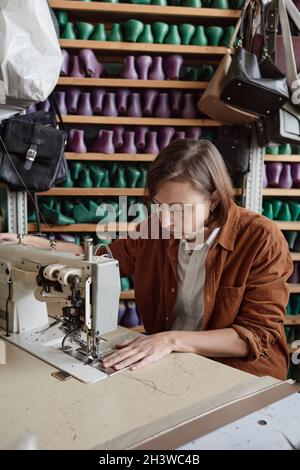 Seamstress concentrating on sewing, she using sewing machine in her work in the workshop Stock Photo