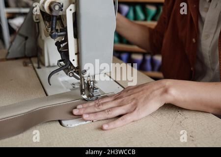 Close-up of seamstress sitting at the table and sewing clothes on sewing machine Stock Photo