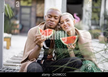 Multiracial couple eating watermelon in their yard Stock Photo