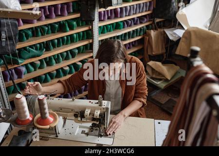 Woman sewing piece of fabric on sewing machine during her work in tailor workshop Stock Photo