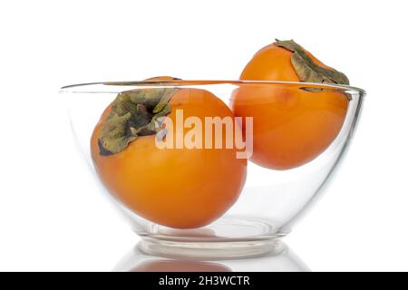 Two ripe sweet persimmons in a glass bowl, close-up, isolated on white.
