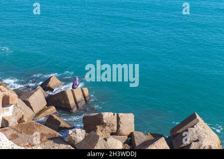 Alexandria, Egypt - December 14, 2018:  Fisherman seats on concrete breakwater in port of Alexandria Stock Photo