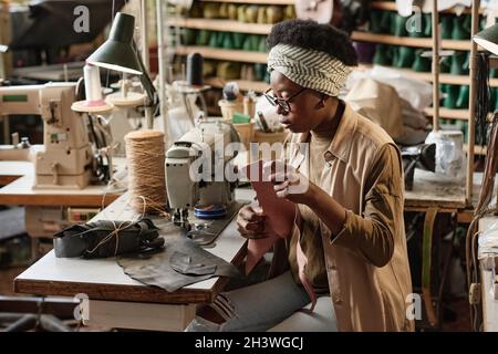 African seamstress sewing two pieces of fabric together on sewing machine at her workplace in the workshop Stock Photo