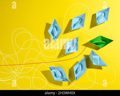 A group of blue paper boats and one green with paths on a yellow background. The concept of a strong leader with extraordinary t Stock Photo