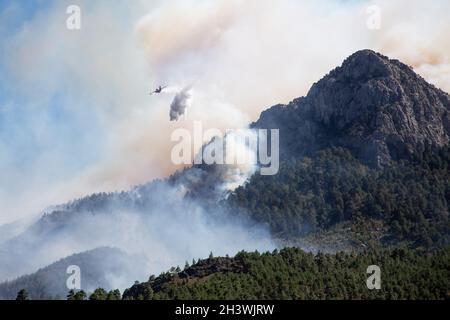 Forest fire extinguisher plane drops water on a forest fire in a steep, rocky terrain. Smoke covered the sky. Stock Photo