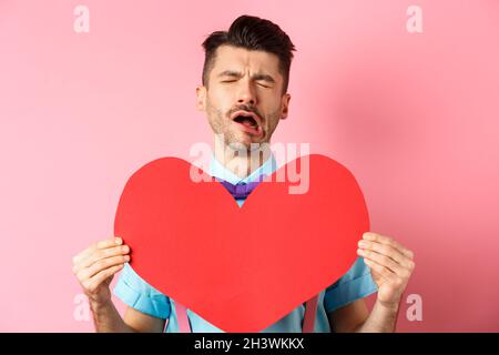 Valentines day concept. Sad and lonely man feeling heartbroken, being rejected, showing big red heart cutout and crying from bre Stock Photo