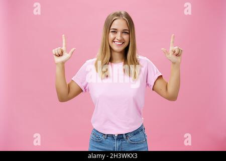 Indoor shot of pleasant attractive friendly-looking girl with tanned skin in casual t-shirt and jeans raising hands pointing up Stock Photo