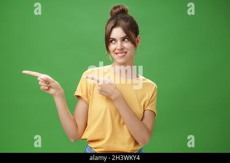 Waist-up shot of charismatic happy and carefree charming woman in yellow t-shirt pointing and looking left enthusiastic and plea Stock Photo