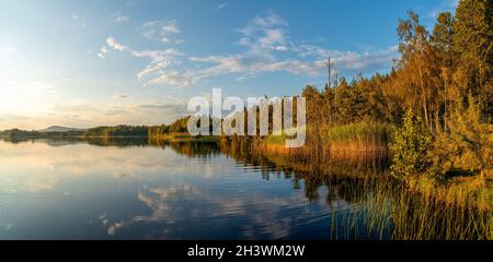 An autumn lake landscape panorama with reflections in the water and warm evening light shining on the forest on the shore Stock Photo