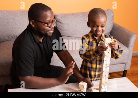 Preschool age boy at home building with wooden puzzle blocks, father encouraging him Stock Photo