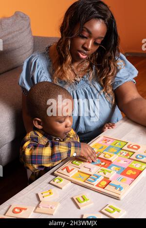 Preschool child at home with mother, playing with alphabet puzzle with mother's encouragment Stock Photo