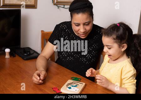 Preschool child, age 4, at home with mother playing with new wooden layered puzzle, excited and interested in activity Stock Photo