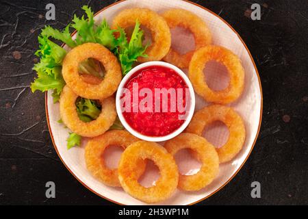 Calamari rings close-up on black. Squid rings with green salad leaves Stock Photo
