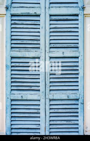 Old blue shutters on the light wall of the house. Stock Photo