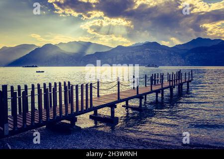 Summer holiday: Wooden dock pier over blue lake water. Cloudy evening scenery. Stock Photo