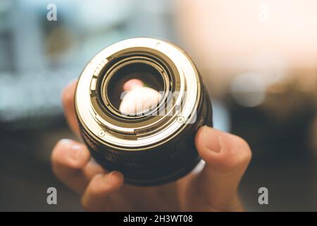 Photographer is holding a photography lens in his hand, laptop in the blurry background Stock Photo