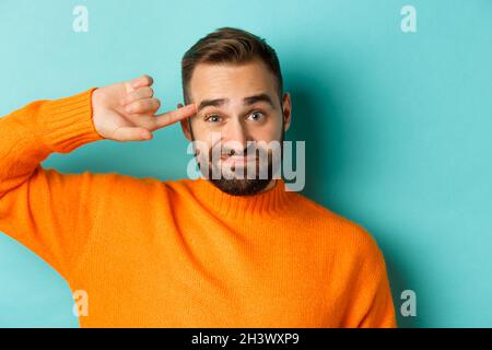 Close-up of man expressing disdain, scolding person, pointing finger at head and looking at camera, standing over light blue bac Stock Photo