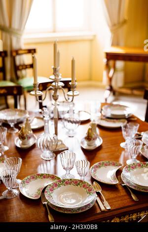 Festive table setting with clean empty plates, spoons, knives, wine glasses, decanters and a candlestick in the center on a wood Stock Photo