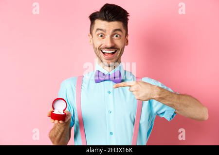 Valentines day. Cheerful young man going to make proposal, pointing finger at engagement ring and smiling excited, standing on r Stock Photo